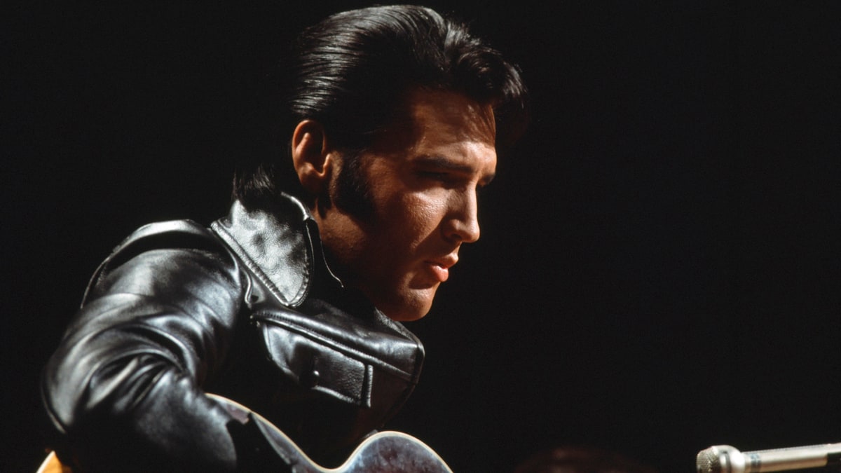 Elvis Presley in a black leather jacket playing guitar on stage