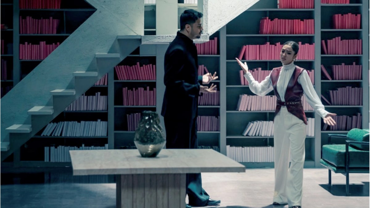 Maanu and Zoha Waseem arguing in a library set with red books in the Shabnam music video Maanu and Zoha Waseem in a still from the Coke Studio Nu.WAV video for Shabnam